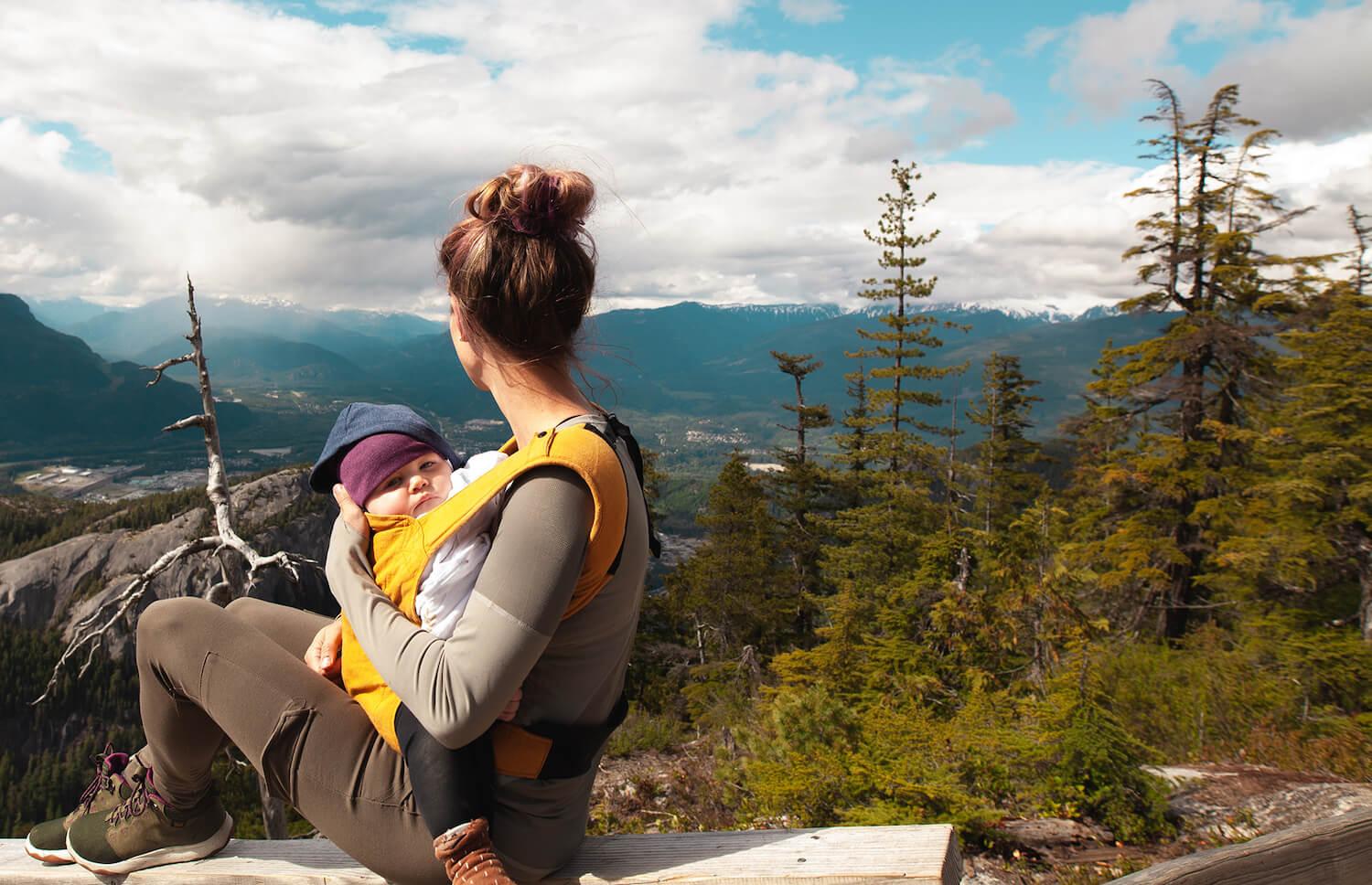 a woman sitting on a bench with a baby in her arms, looking at the landscape behind them