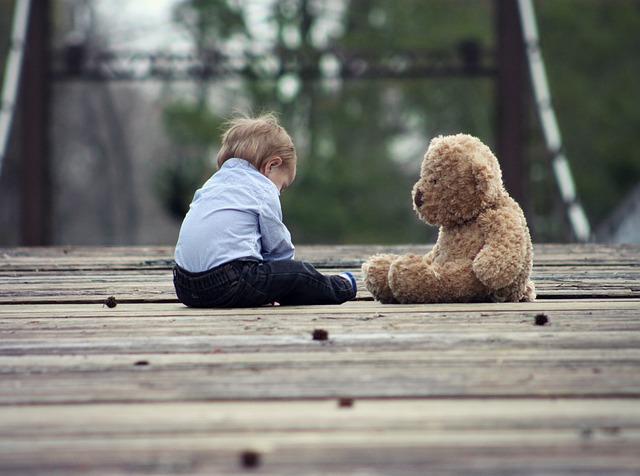 a child sitting on a bridge next to a teddy bear stuffed animal