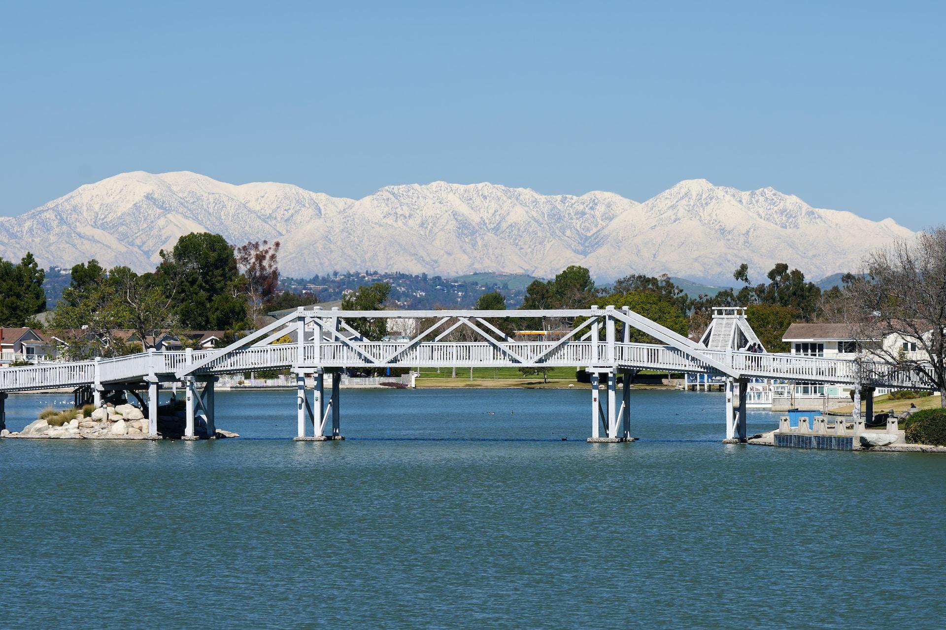 a wood bridge over a body of water with snow-covered mountains in the background