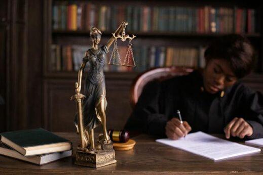 a judge writing at her desk next to a lady justice statue
