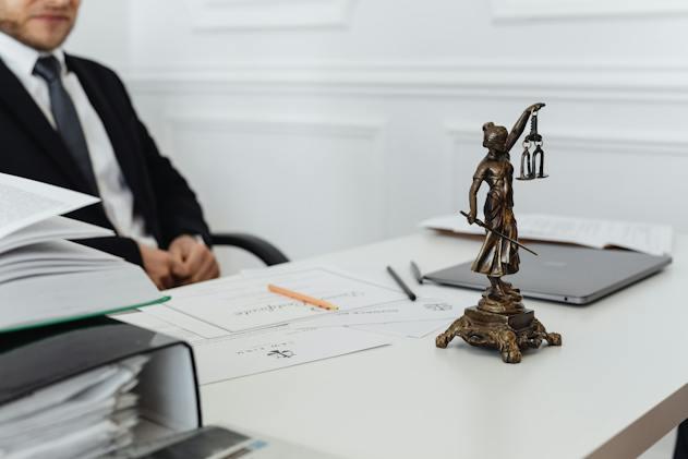 a man in a suit sitting at his desk, which prominently features a lady justice statue