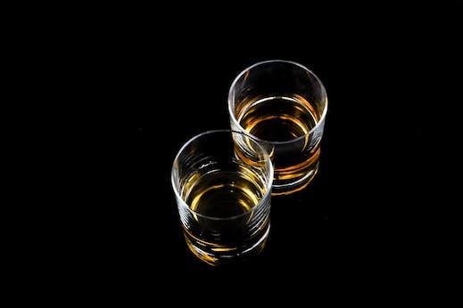 two glasses of alcohol against a black background