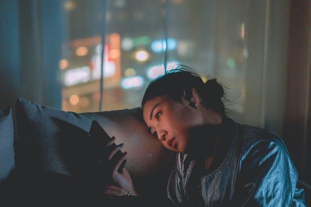 a woman sitting on a couch in dim lighting and looking at her phone
