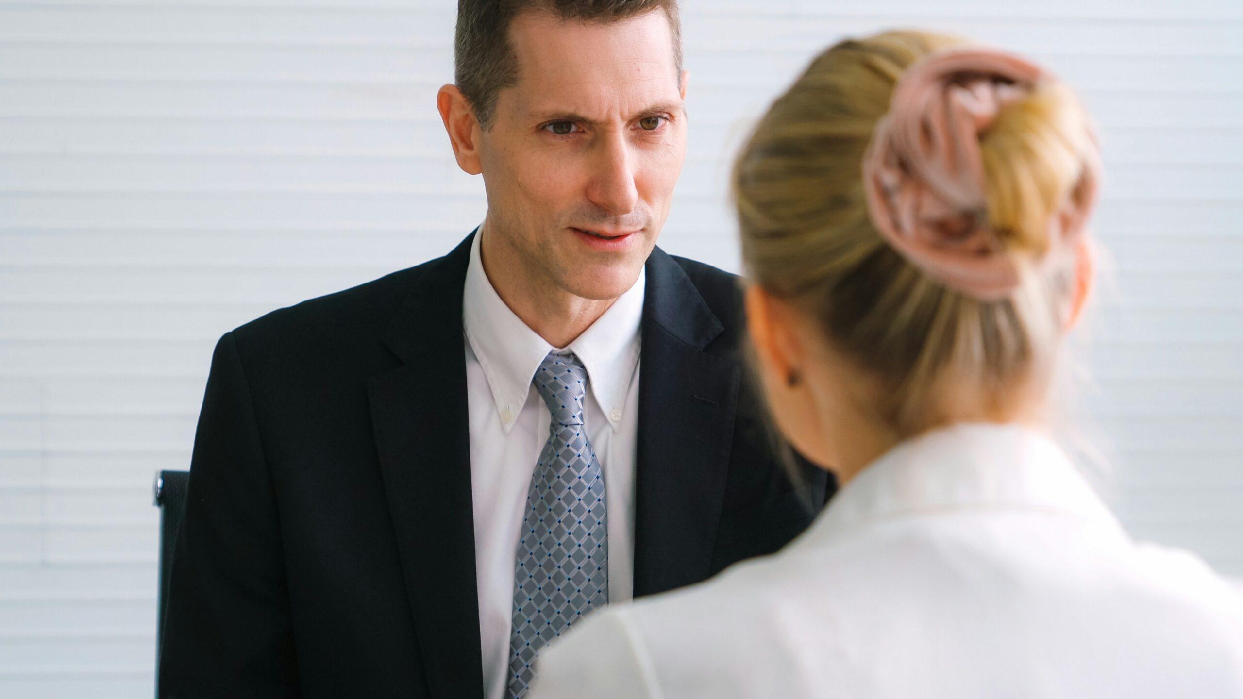 A man in a suit converses with a woman in a professional setting.