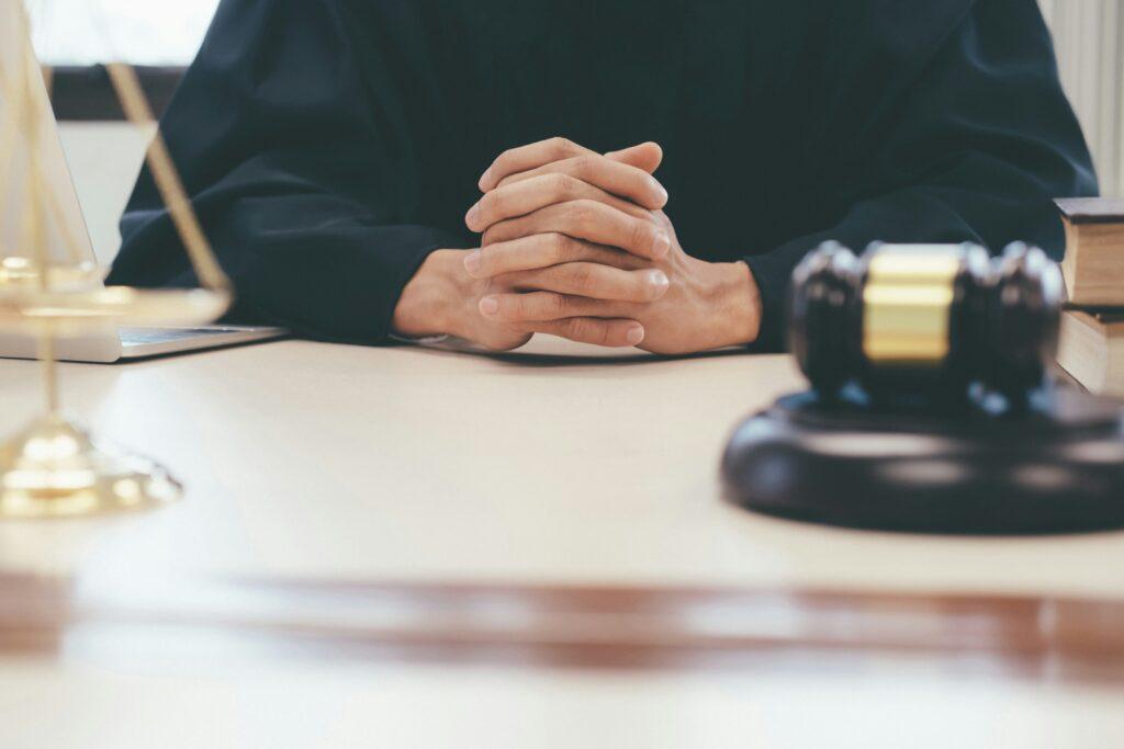 A judge seated at a desk, holding a gavel, with a scale of justice prominently displayed beside them.