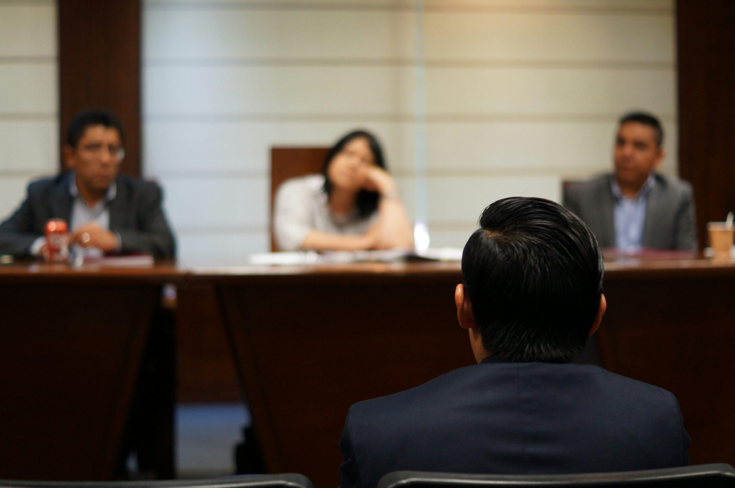 A man seated at a conference table in a meeting room, engaged in discussion with others.