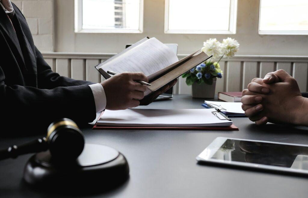A man in a suit sitting a a desk and a holding a book.